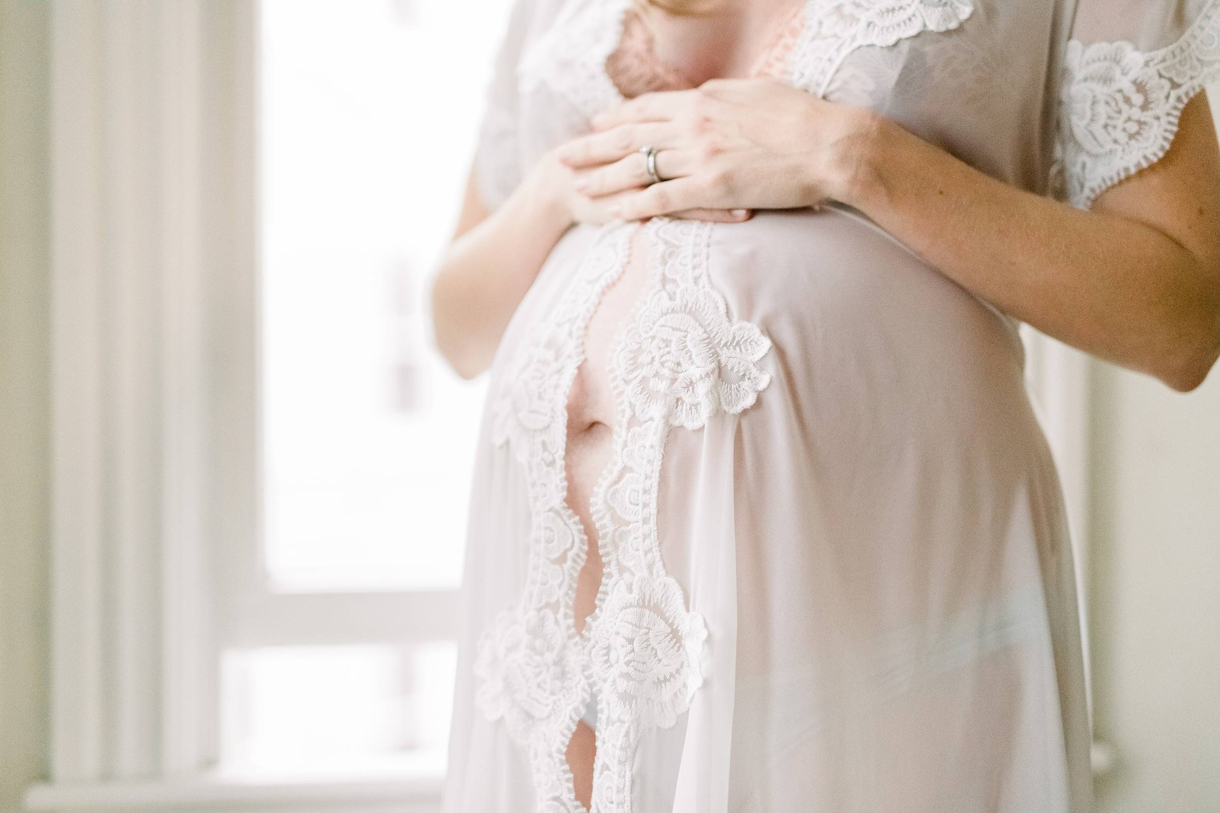 Pregnant woman in sheer robe with hands resting on her belly
